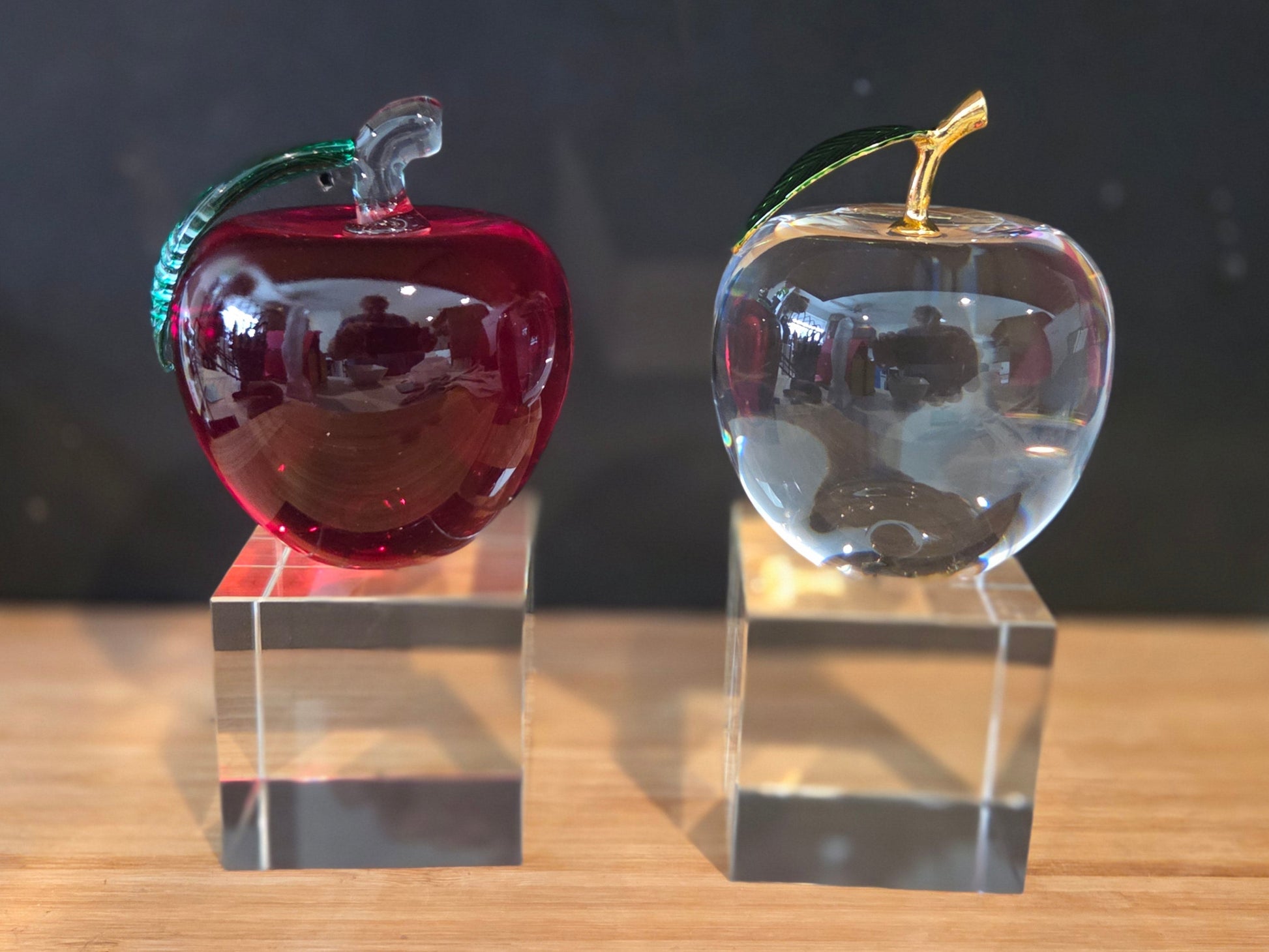 Two glass apples, one red and one clear, on transparent bases
