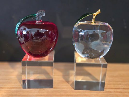 Two glass apples, one red and one clear, on transparent bases